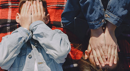 A top shot of two kids laying down beside each other while covering their faces