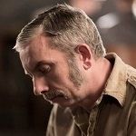 Warren Glover - A side view image of a middle aged man with a golden brown hair looking down while wearing a brown polo