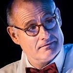 Steve Allnutt a middle aged man wearing a round glasses, white polo and a red tie ribbon.