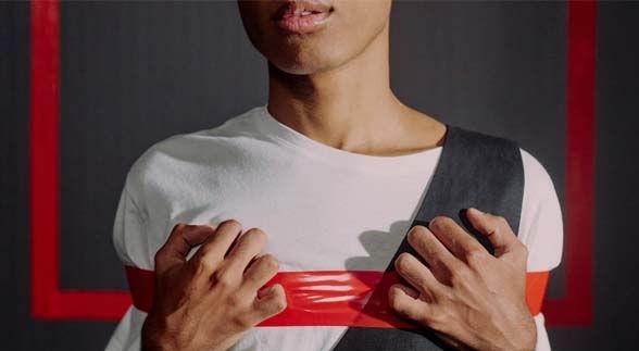 A man showing only his mouth and half body wearing a white shirt with black shawl and red tape around his shirt.