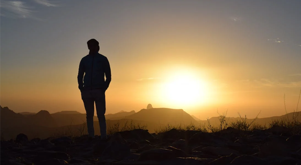 A silhouette of a man standing in a cliff in front of sunrise