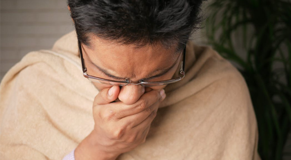 Male wearing a glasses and a hoodie in a coughing gesture