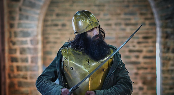 A bearded knight wearing a gold armour and helm
