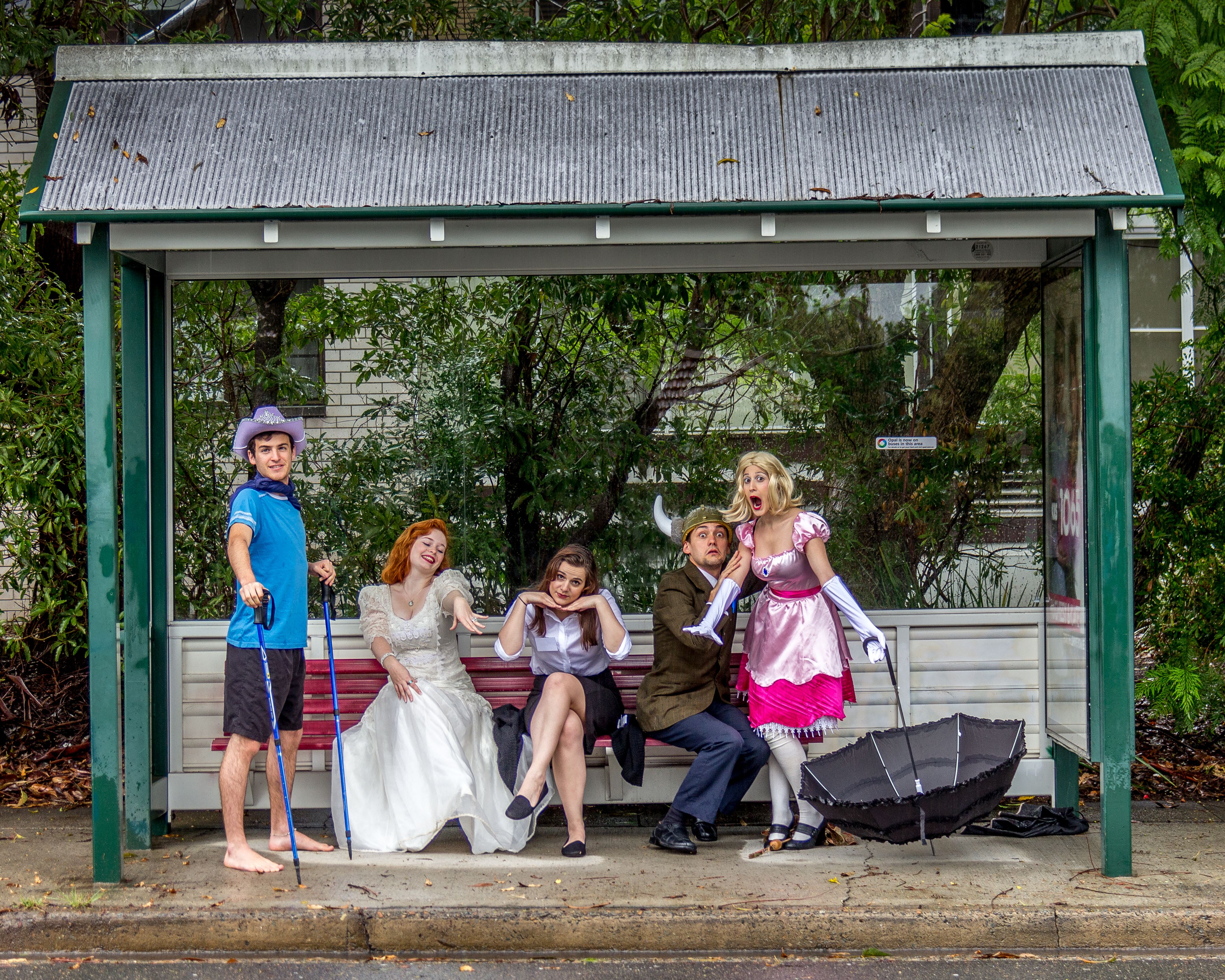Five actors sitting on a bench doing a wacky pose in a group image