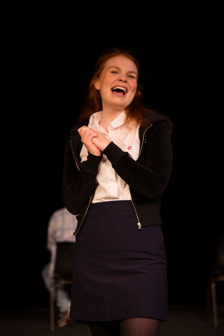 Smiling Blonde girl wearing a white polo, black jacket and navy blue skirt