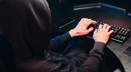 A man in a black hoodie typing at his keyboard