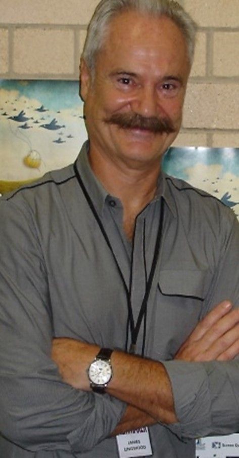 James Lingwood - A middle aged man with white hair and a fully grown moustache wearing a grey polo