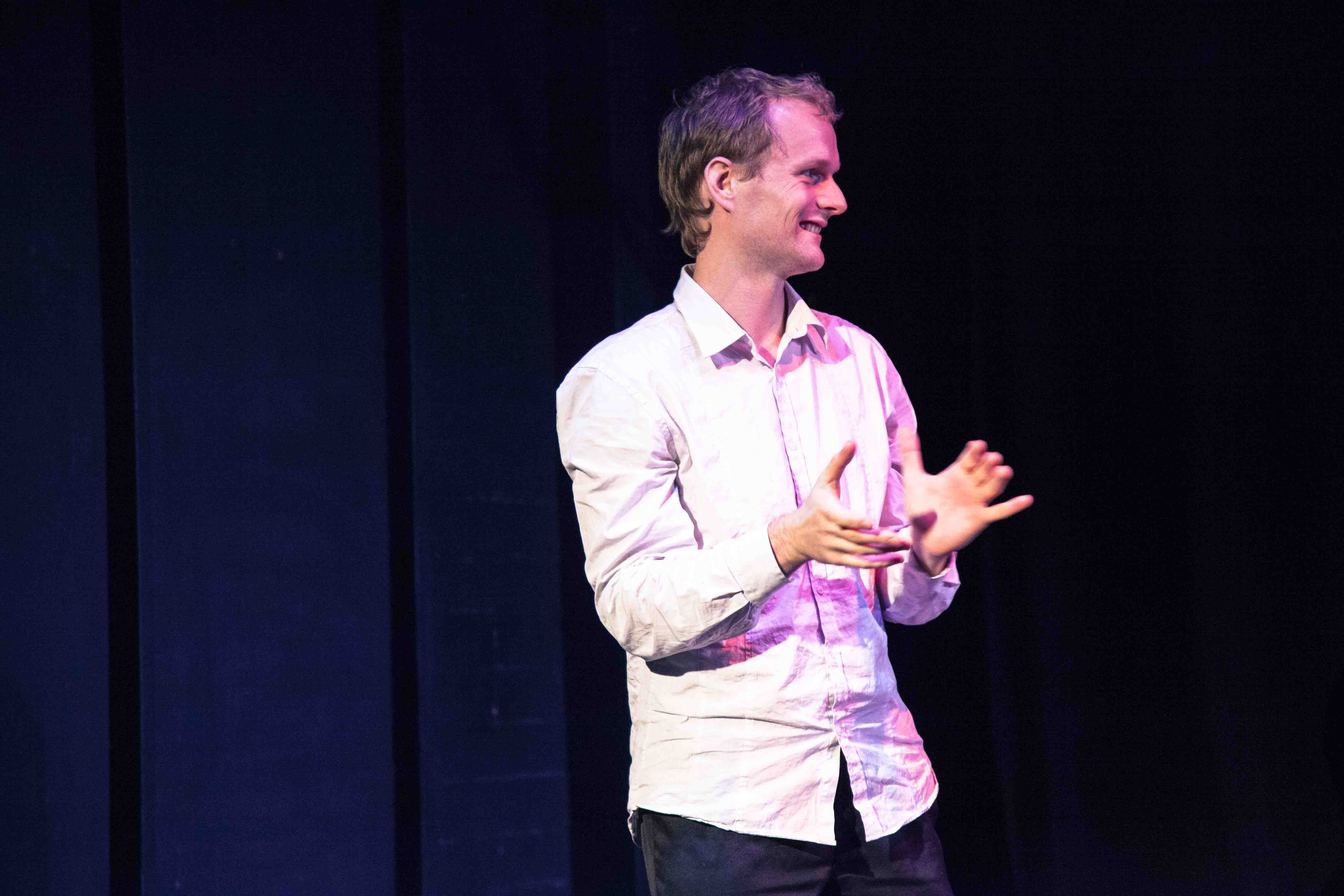 Pete Malicki, smiling on stage doing a hand gesture