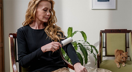 A middle aged Blonde woman cleaning her clothe with a pet hair removal roller