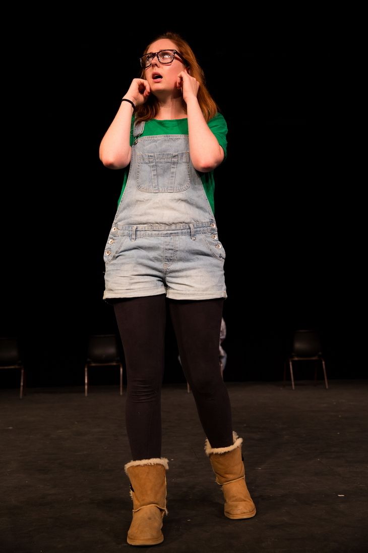 Standing blonde girl wearing a glasses, green shirt with a jumper and a brown boots