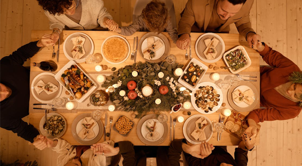 A family holding each other hands and sitting in a dining table with a lot of food