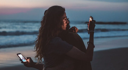 Two couples hugging each other while both are looking at their phones at the same time