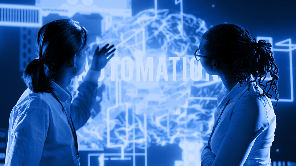 Two female scientist looking at a futuristic technology that says "Automation"