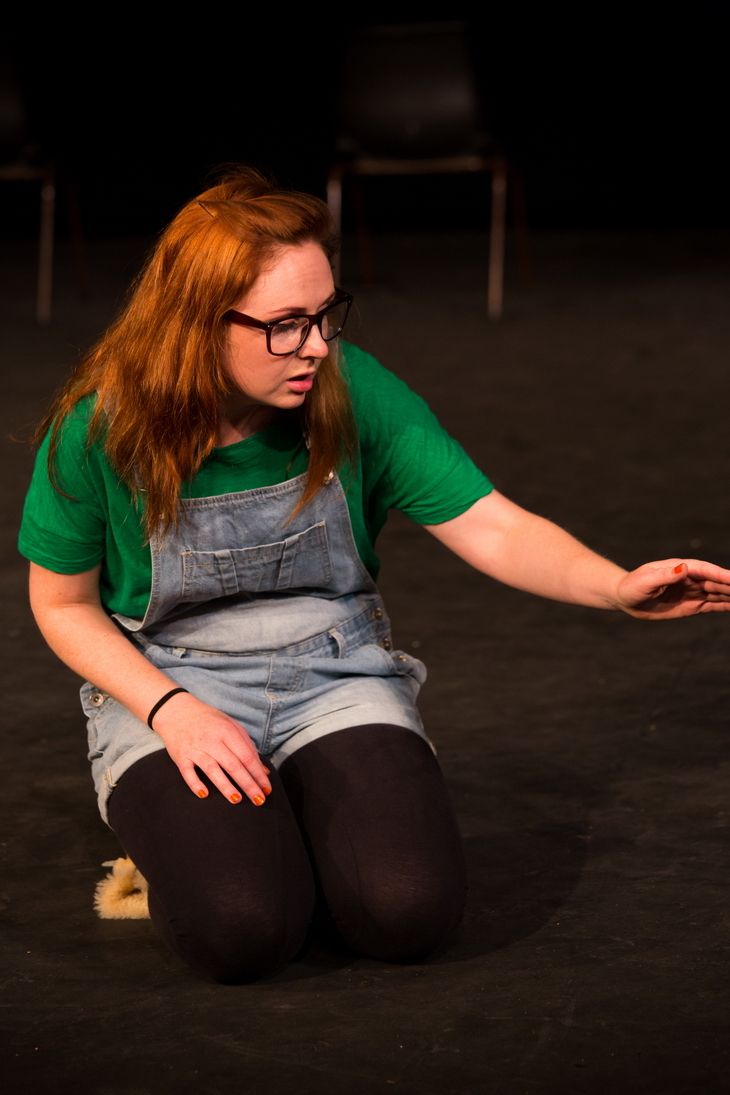 Kneeling blonde girl wearing a glasses, green shirt with a jumper.