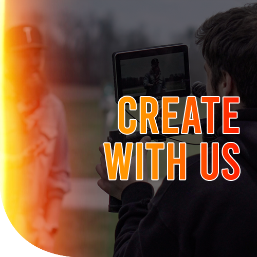 A male filming a bearded guy wearing a cap and a denim jacket in a park