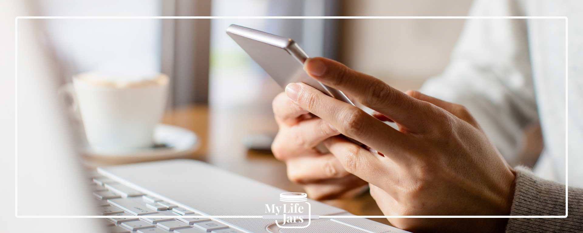 A picture of a man at a computer and holding a mobile phone in his hand