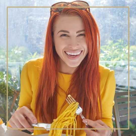 girl in yellow jumper with ginger long hair eating spaghetti from a fork