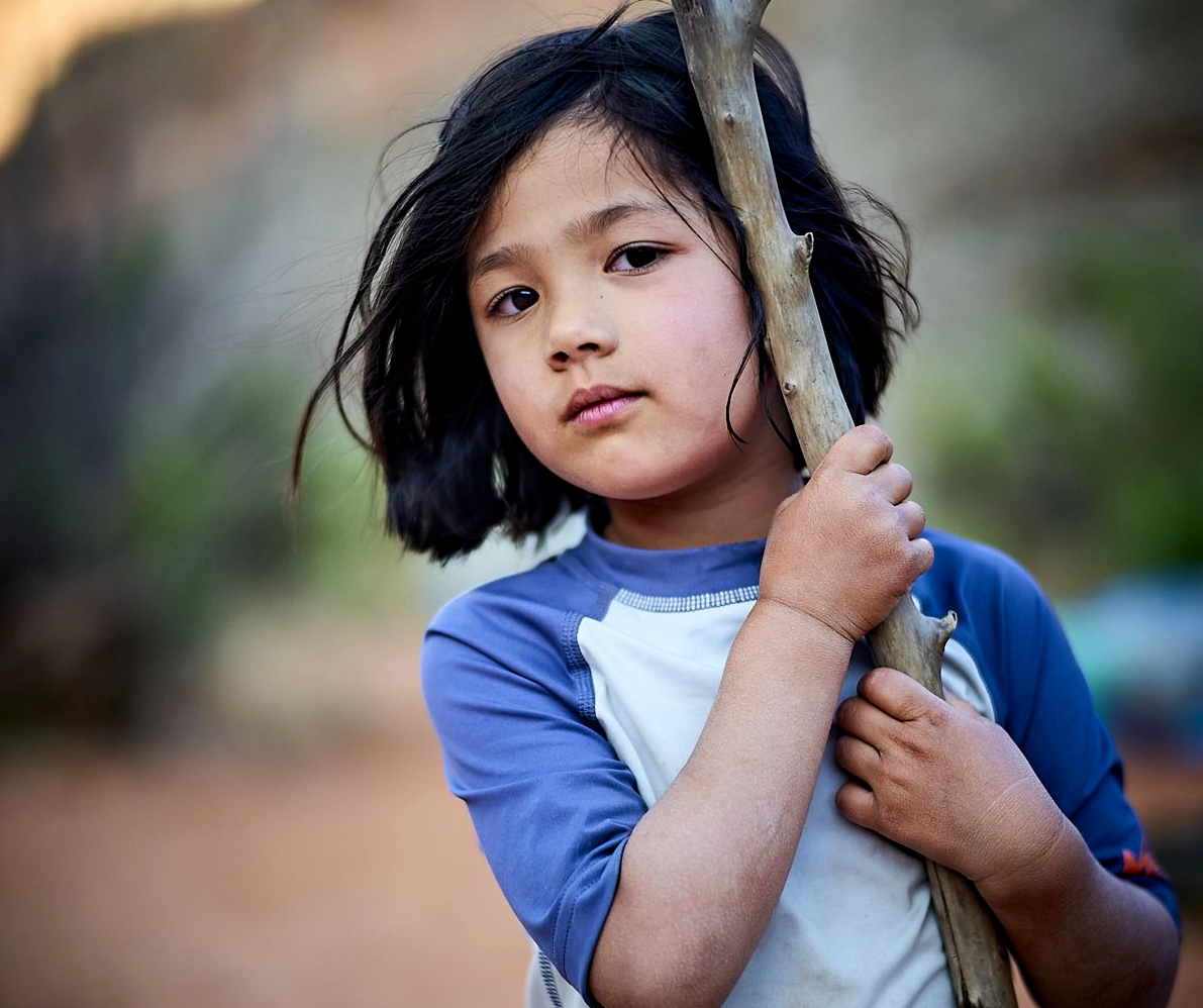 Carys holds a Y-shaped stick over her shoulder, looking directly at the camera with a thoughtful expression