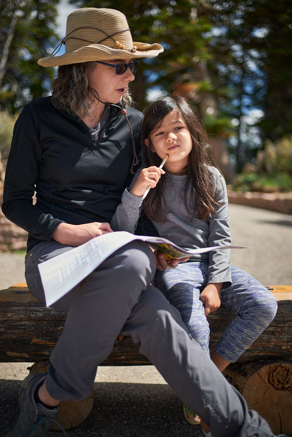 Jen Lumanlan in sun hat sitting on wooden bench with daughter Carys, reading together outdoors in relaxed moment showing positive parent-child connection