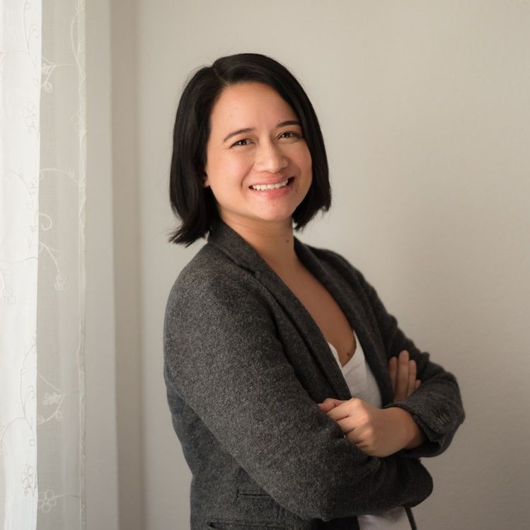 Carys stands smiling on a snowy mountainside wearing a pink fleece jacket, with snow-capped peaks and blue sky behind her.