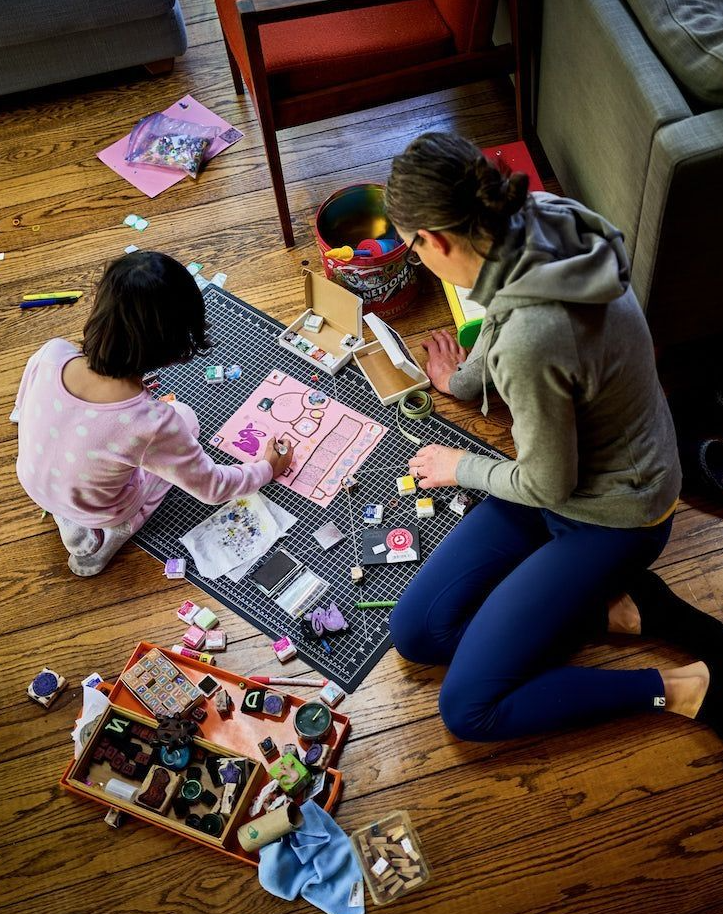 Overhead view of parent Jen Lumanlan and daughter Carys sitting on a wooden floor working on an art project together