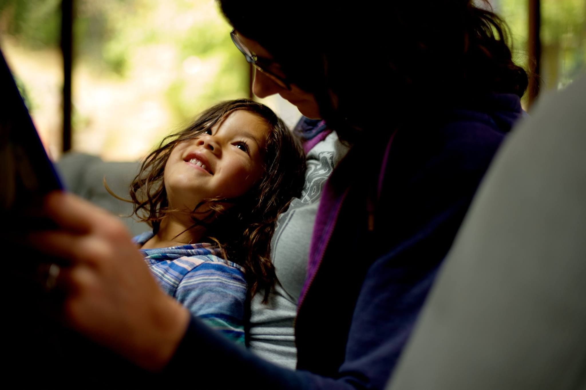 A young child with wavy dark hair looking up with a joyful smile at an adult who is wearing glasses