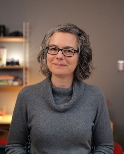 Jen Lumanlan, parenting coach and host of Your Parenting Mojo podcast, smiling at camera wearing glasses and grey sweater