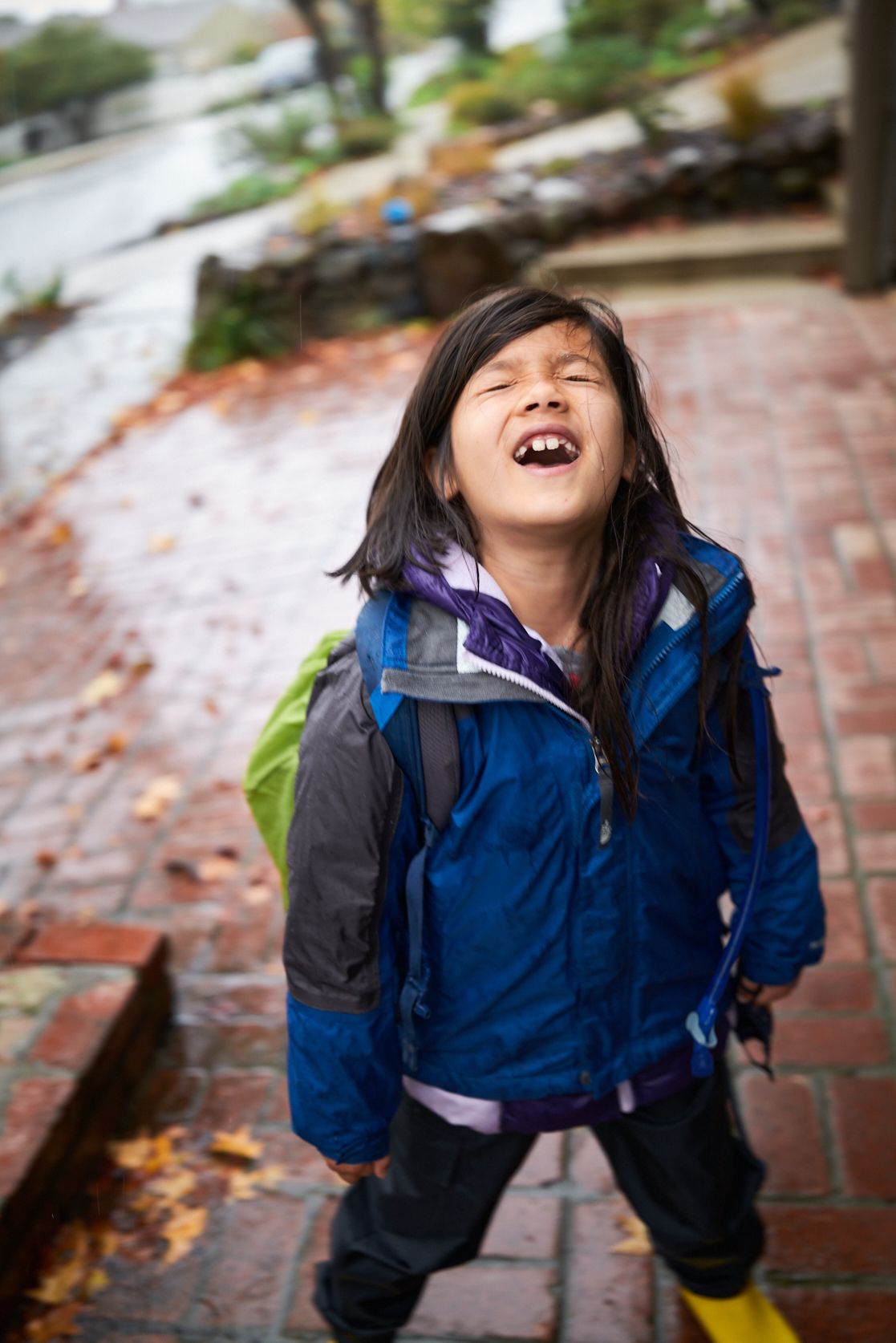 Carys Lumanlan laughing with pure joy outdoors in blue jacket and backpack, demonstrating the happiness of children raised with respectful parenting approaches