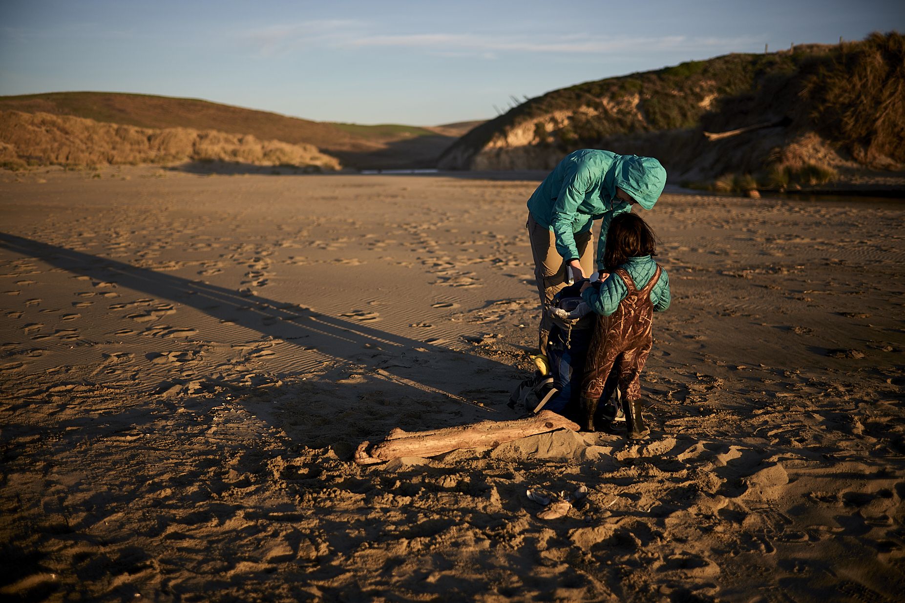 Parent and child discovering driftwood together on a beach at sunset