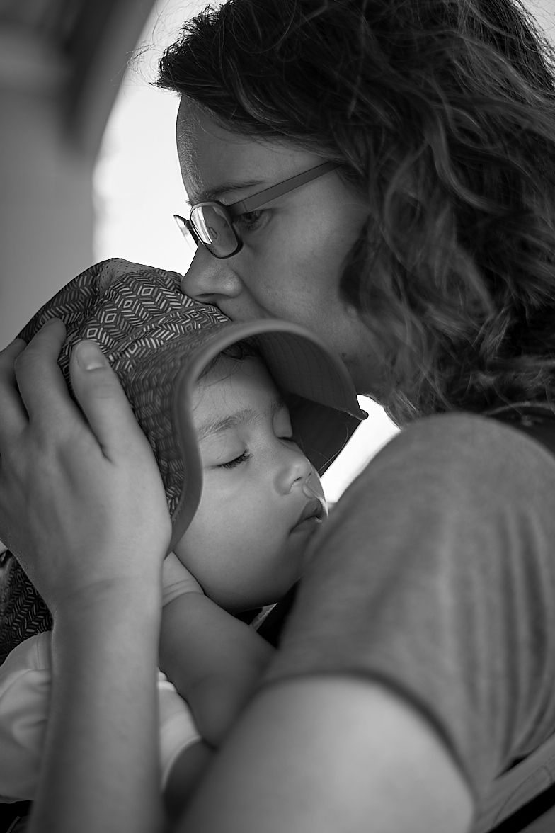 Black and white photo of a mother with glasses and curly hair holding and gently touching the face of her young child who appears peaceful and content
