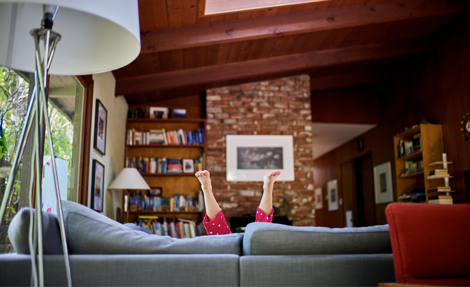 Child's legs in red polka dot pajamas stretched up behind a gray couch in a warm, book-filled living room