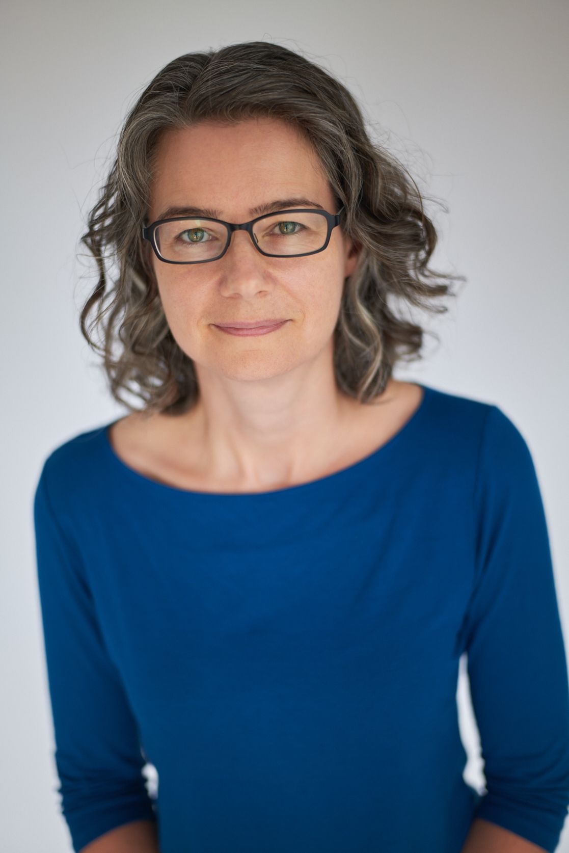 Professional headshot of Jen Lumanlan, parenting coach and Your Parenting Mojo podcast host, wearing blue top and glasses against neutral background