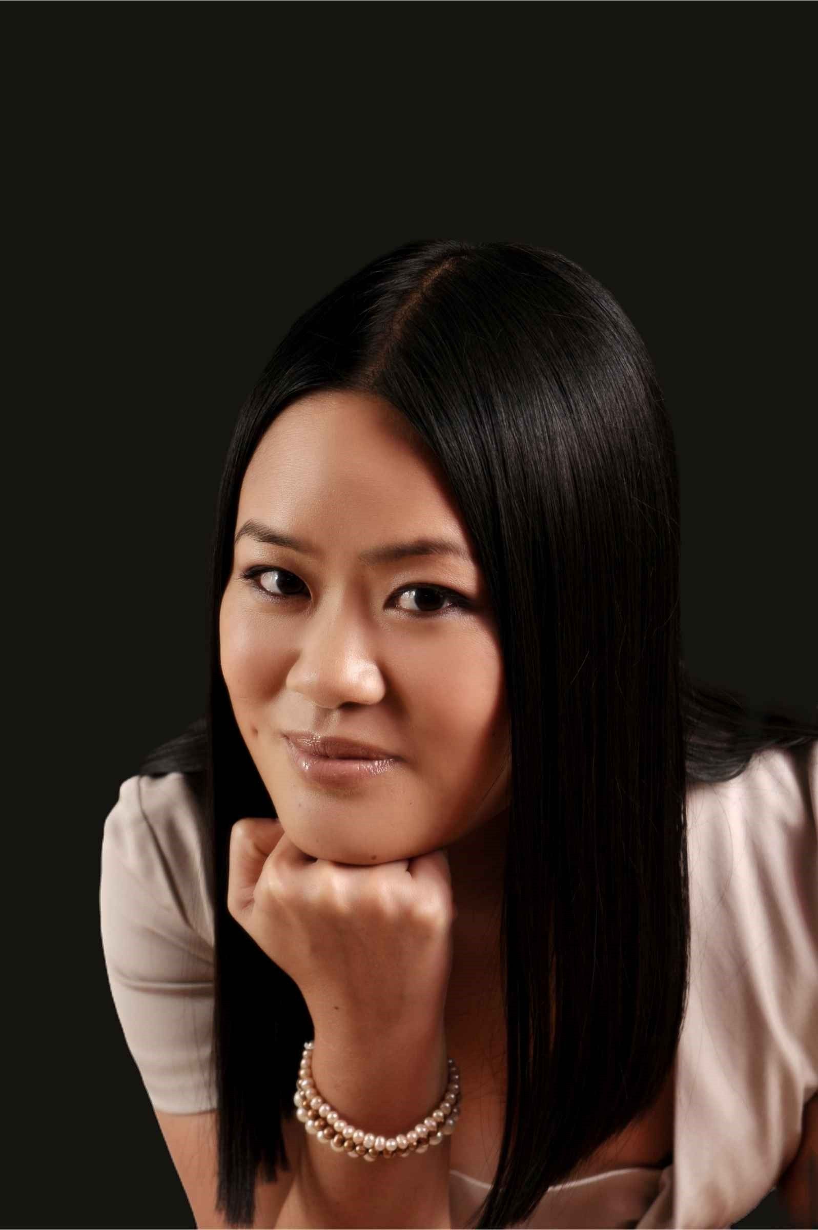 A woman with long dark hair resting her chin on her hand, against a dark background