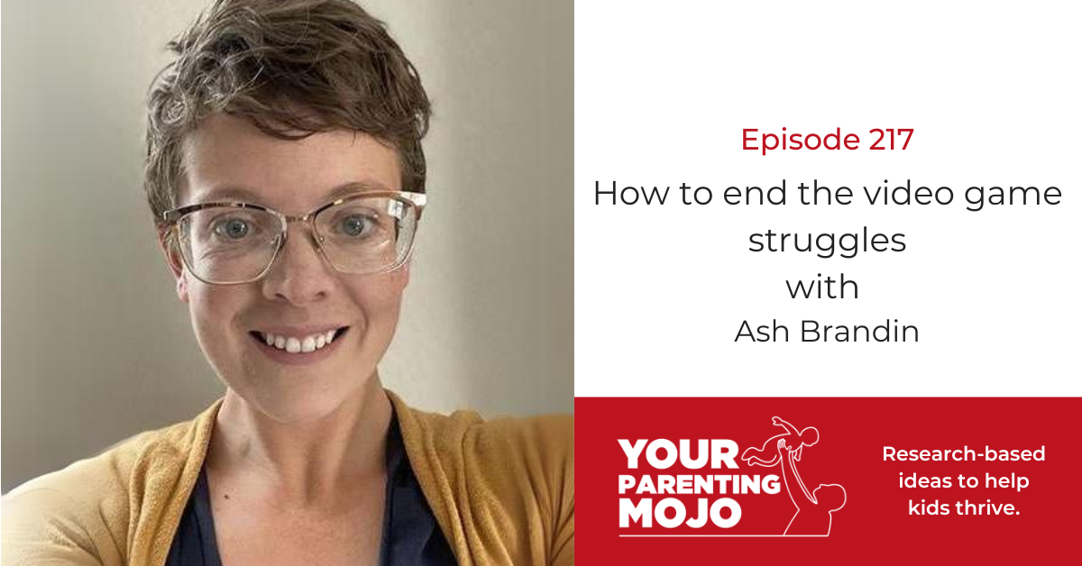 a person with short brown hair and glasses wearing a yellow cardigan, smiles at the camera