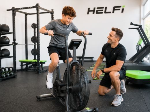 Youth cardio and conditioning support at Helfi gym in Woolloongabba Brisbane with a teenager using an air bike under trainer supervision.