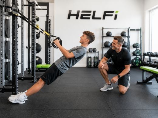 Safe supervised age-appropriate youth training at Helfi gym in Woolloongabba Brisbane with a trainer guiding a teenager through resistance band exercises.