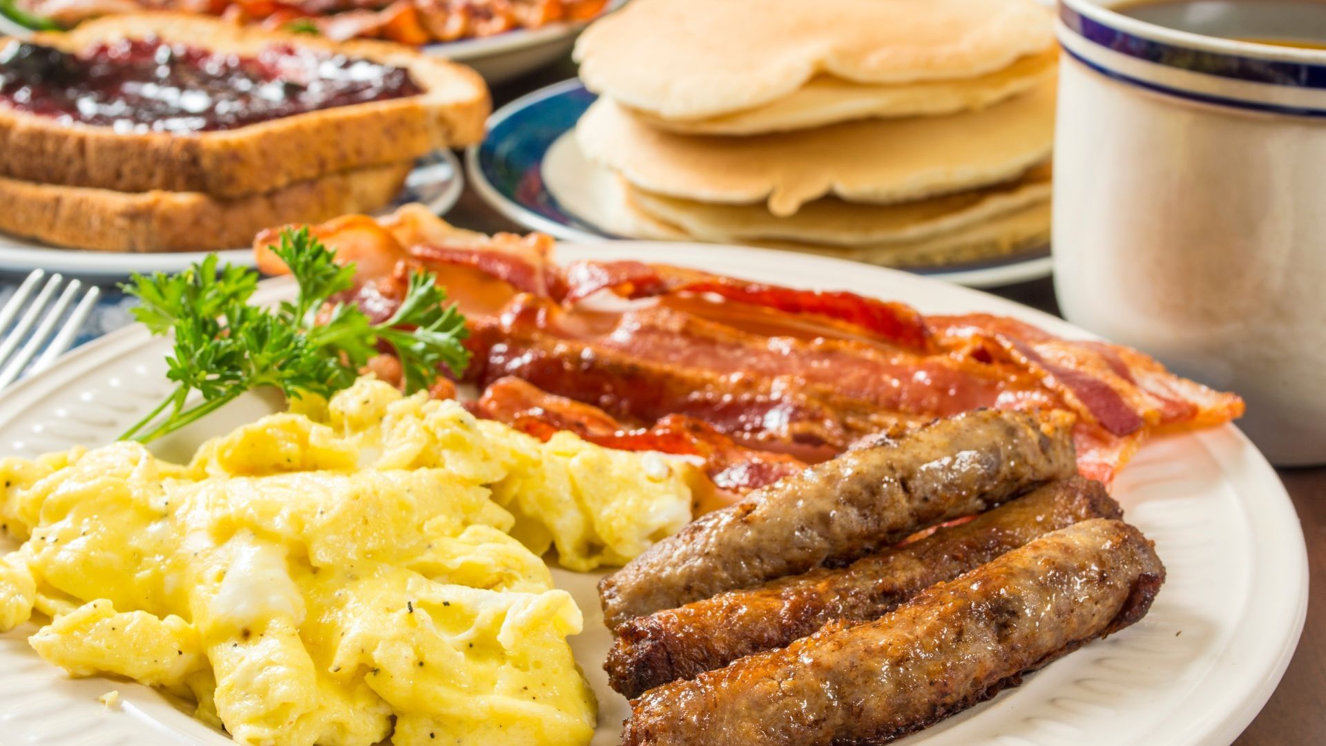 A large breakfast spread including scrambled eggs, bacon, sausage, toast with jelly, and pancakes. 