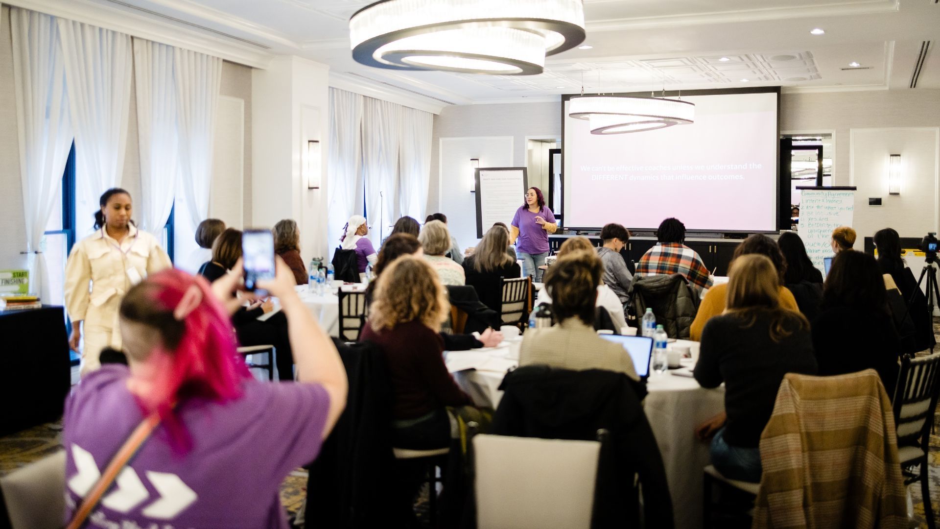 A large group of people are watching Trudi Lebron deliver a presentation at The Coaches Forum. 