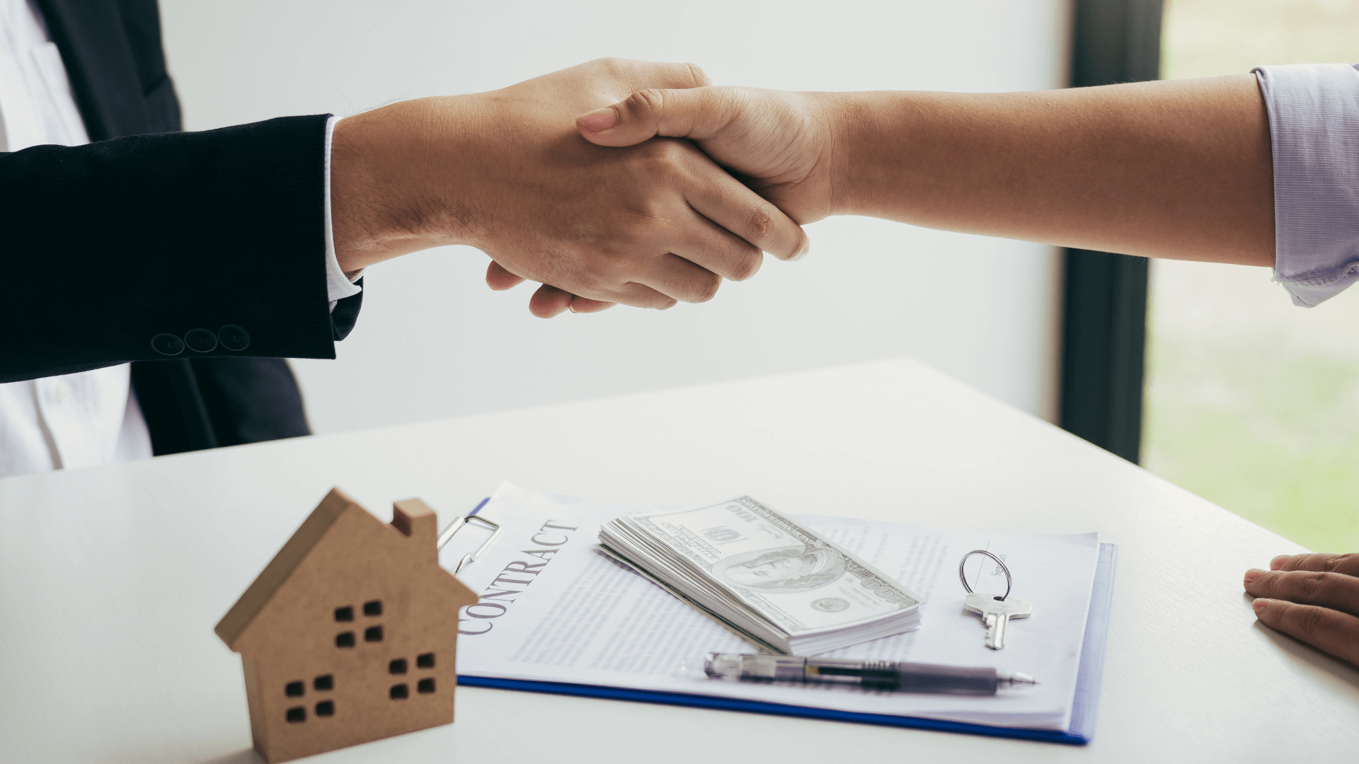 Two individuals shaking hands over a set of property blueprints, symbolizing the finalisation of a commercial property deal.
