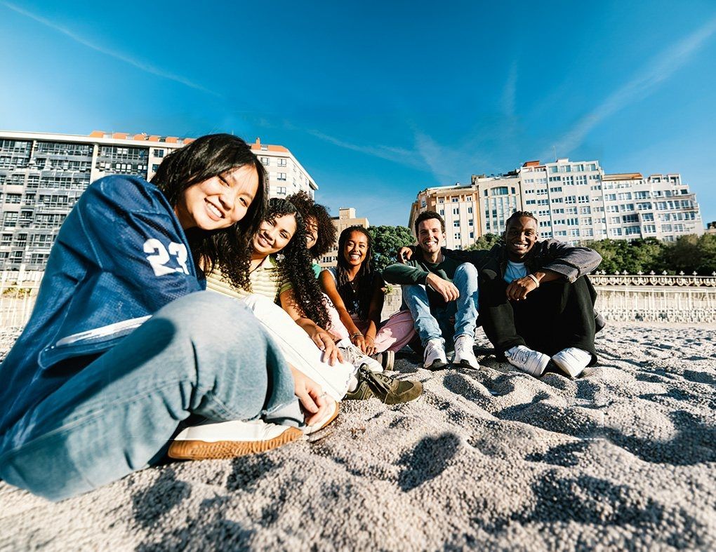 Young people sitting together on a sunny beach in front of city buildings