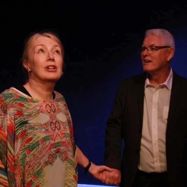 Male and female standing in front of dark background while holding hands