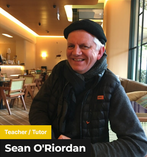Sean O'Riordan - Smiling Old man with white hair wearing a black beret, black scarf and black puffer jacket 