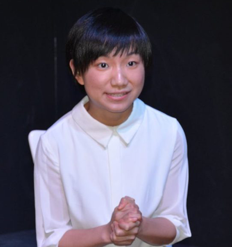 A dark haired Girl wearing a white polo speaks in an acting class