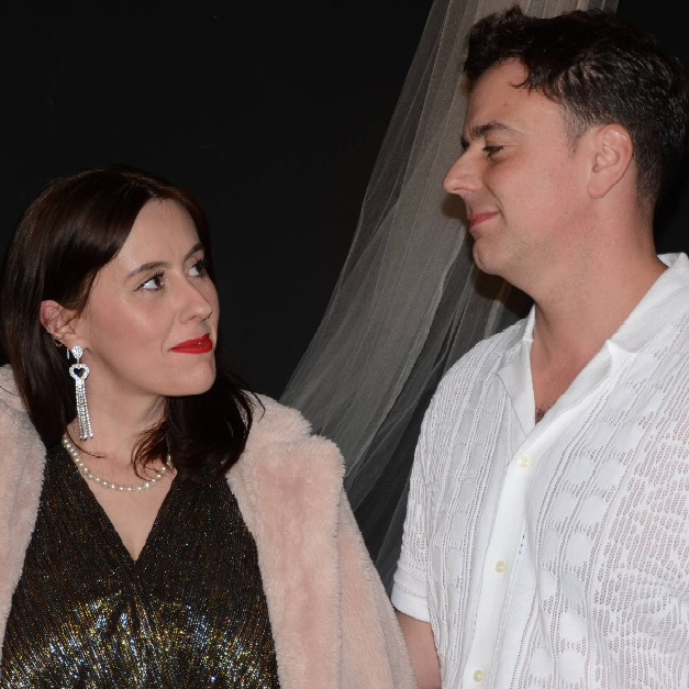 Male and female standing in front of dark background while holding hands