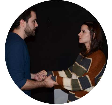 Male and female standing in front of dark background while holding hands