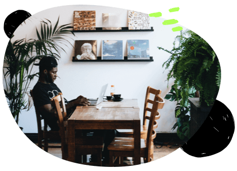 A man sitting at a wooden table flanked by green plants with vinyls on the wall behind him.