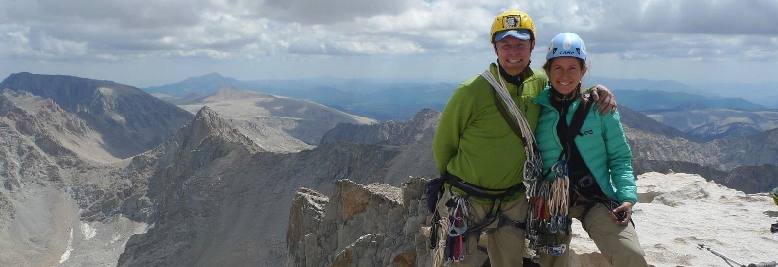 A male and female climbers at the top of a snowy mountain peak.